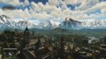 Dying Light The Beast screenshot showing panoramic view of Castor Woods with snow-capped mountains, medieval buildings, and rural landscape under cloudy sky