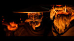 Two characters wearing Japanese-style masks with multiple eyes and oni-like features, illuminated by warm orange light against a dark background in Ghost of Yotei.