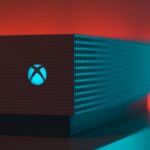 Close-up of an Xbox Series X console with illuminated Xbox logo against a red and teal background