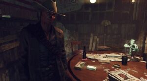 The Ghoul character from Fallout portrayed by Walton Goggins stands in a dimly lit room at The Last Resort, wearing a wide-brimmed hat and duster coat with ammunition belts across his chest, standing beside a table with various wasteland items.