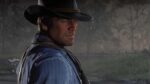 Close-up shot of Arthur Morgan from Red Dead Redemption 2 wearing a cowboy hat and blue shirt against a misty forest background.