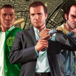 Grand Theft Auto V promotional artwork showing three main characters standing in front of cars and cityscape with dramatic lighting and orange sky background